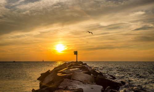 The New Buffalo beach shoreline at sunset. There are clouds and the orange sky shows the sun right above the water.